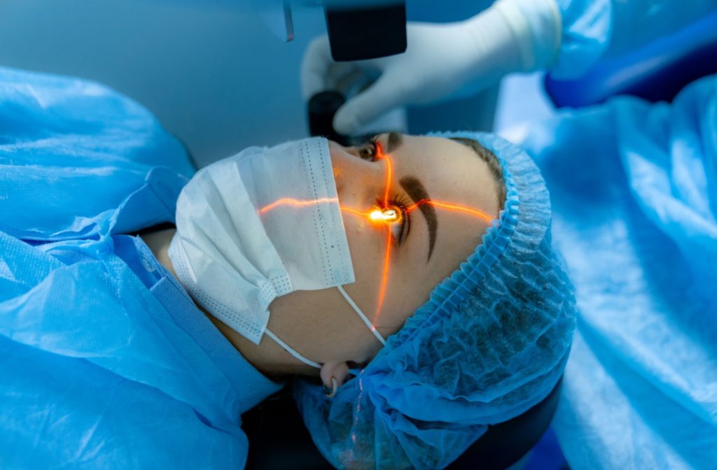 Close-up of a young woman undergoing laser eye surgery. A bright orange laser makes a cross intersecting over her eye