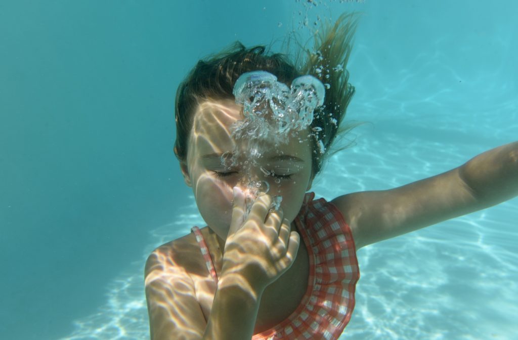 A child underwater in a saltwater pool with eyes closed and holding their breath, enjoying the swimming experience.