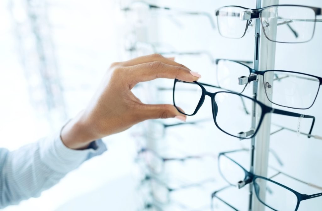 An image of a person selecting which pair of prescription glasses they would like to use, and taking them off of a store shelf.