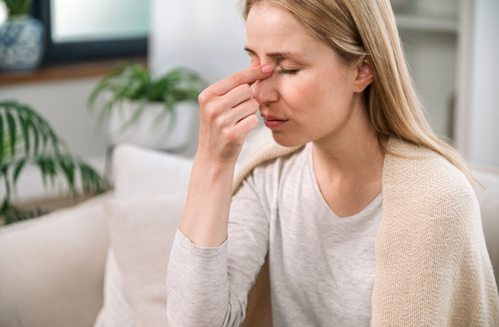 Someone with a sinus infection winces and pinches the bridge of their nose.