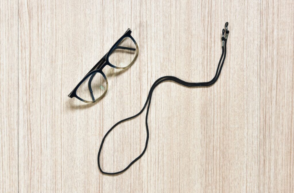 A pair of black prescription glasses and a glasses strap against a wooden background.