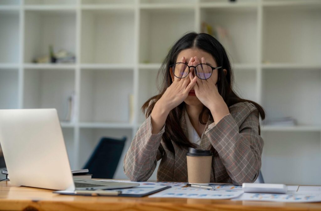 A person in an office with their hands over their eyes under their glasses due to the anxiety they feel.